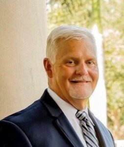 Ron McDonough, wearing a suit, smiles at the camera.