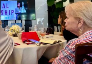 Three people sitting at a circular table look towards a screen.