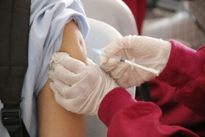 Close up of two gloved hands administering a vaccine to someone's shoulder.