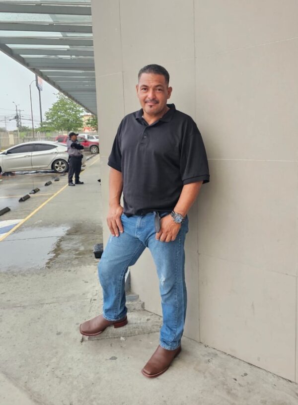 Oscar Romero Santos stands with his hands in his pockets in front of a building.