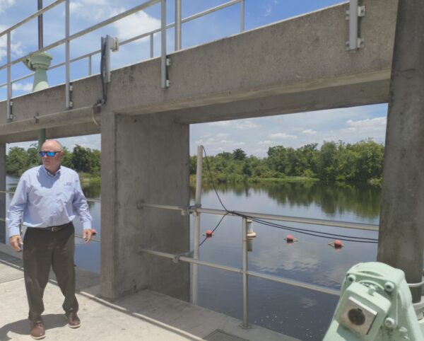 A man stands on a concrete structure, which is open to show a river in the background.