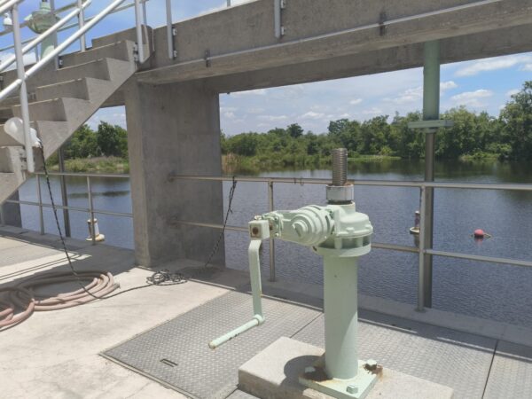 A green hand crank sits on top of a concrete structure, which is open on the sides to show a river in the background.