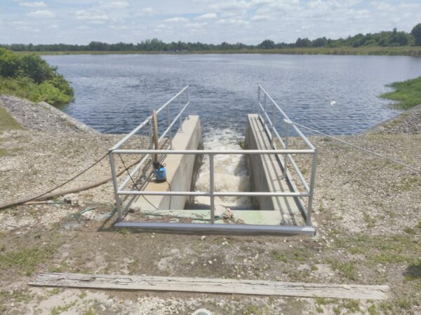 Handrails surround an opening in concrete where a rush of water exits, flowing into a reservoir.