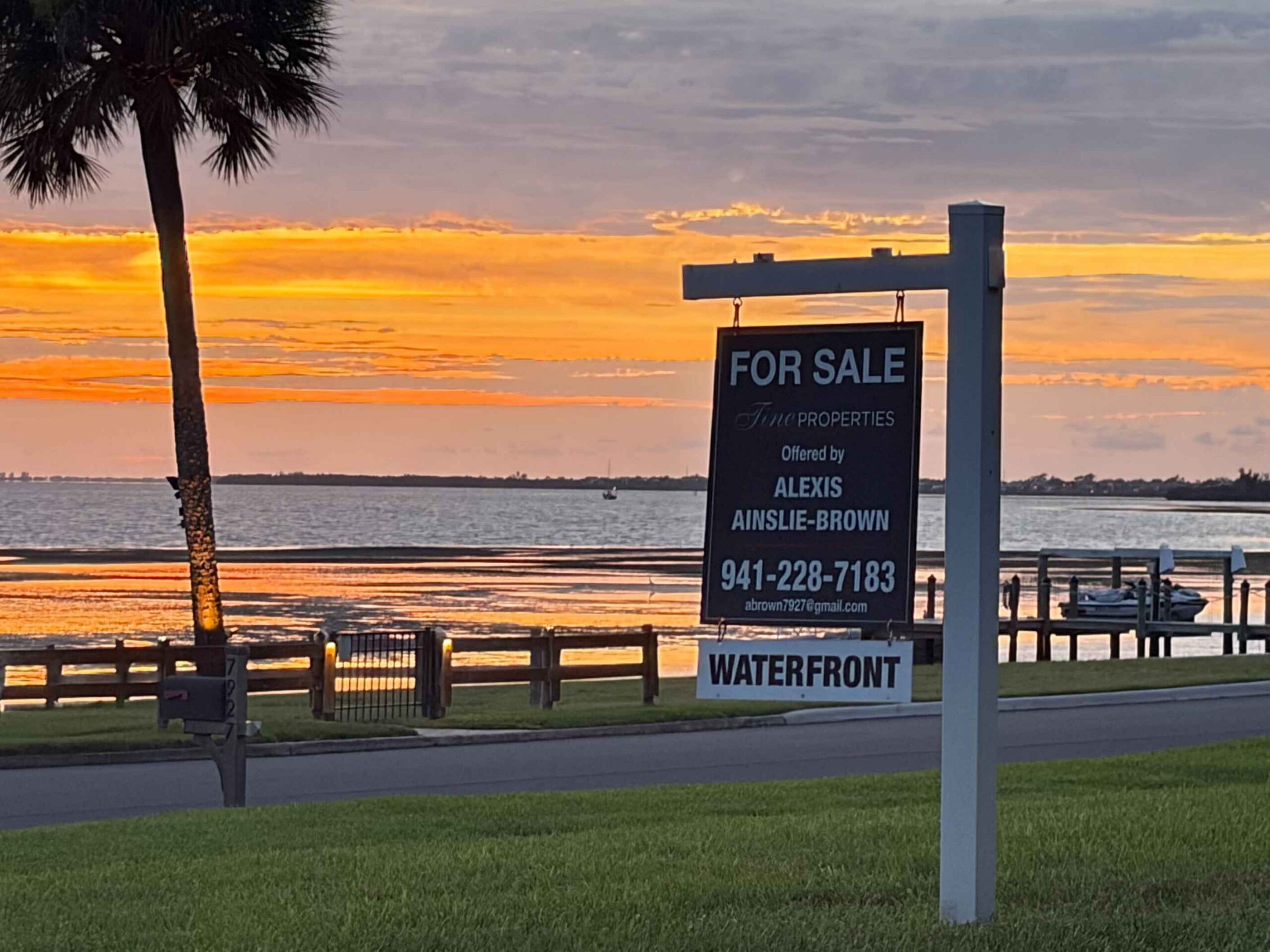 Sunset Real Estate A for-sale sign is illuminated by the setting sun in front of the Sarasota Bay.