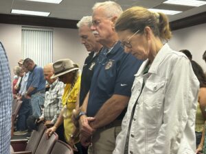 People bow their heads in prayer in crowded room.