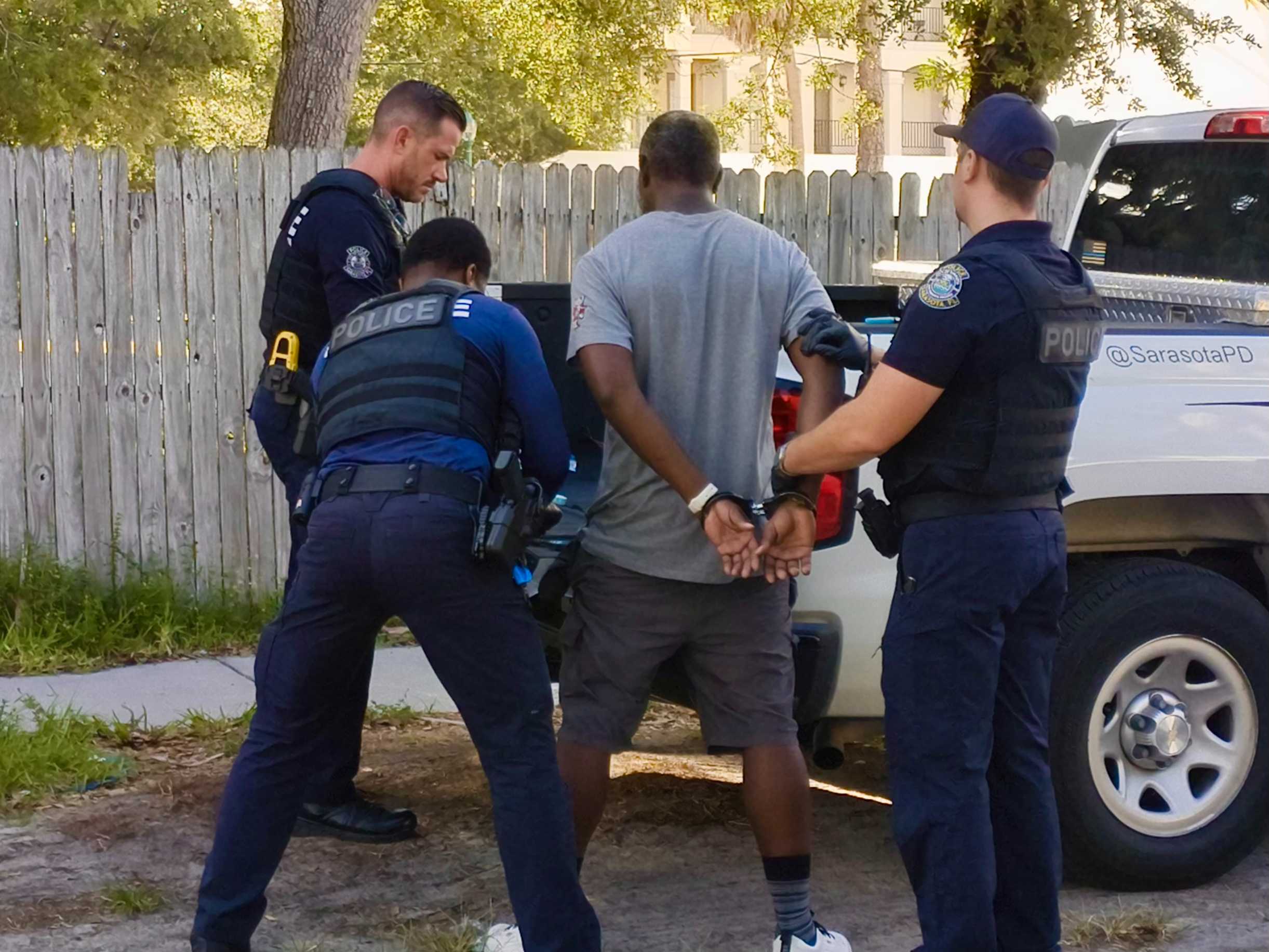 Homeless Arrest Three police officers handcuff a man next to a police squad car.