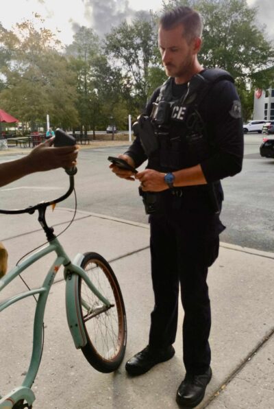 A police officer looks at a phone that someone off-screen is holding in front of him.