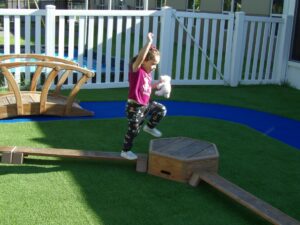 A toddler is in the middle of taking a big step between two pieces of playground equipment
