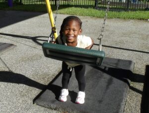 A child leans on a swing while smiling at the camera