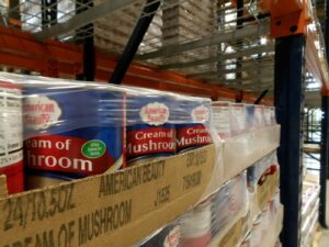 Cans of Cream of Mushroom Soup are stacked on shelves in a warehouse