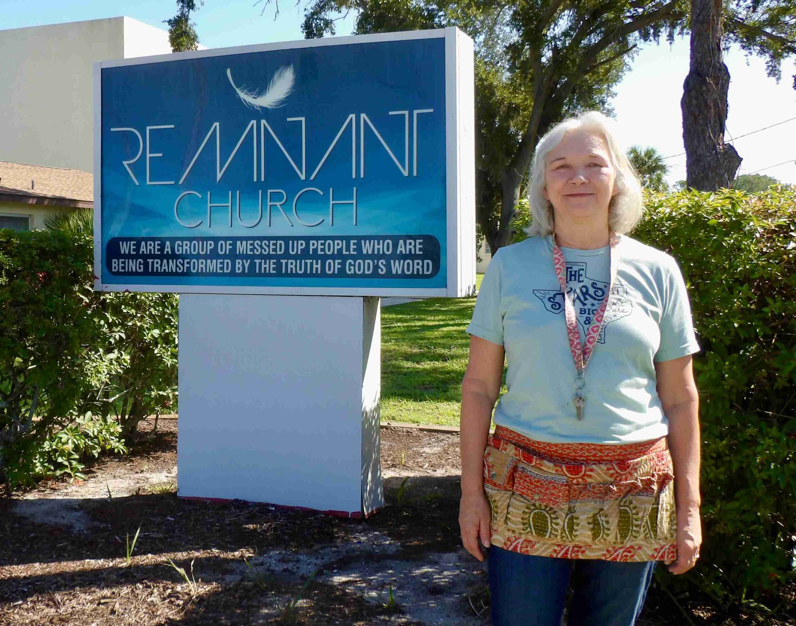 Tammy Burns-cropped-toned2 A woman stands in front of a church sign reading "Remnant Church: We are a group of messed up people who are being transformed by the truth of God's word."